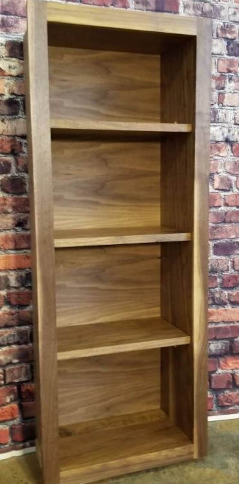 Pu&ograve; includere: Una libreria alta in legno con quattro ripiani. La libreria &egrave; realizzata in legno marrone chiaro e ha un design semplice e rettangolare. I ripiani sono distanziati uniformemente e sembrano robusti. La libreria &egrave; contro un muro di mattoni.