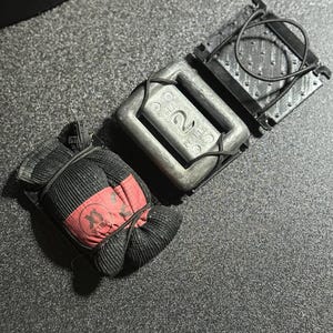 Pode incluir: Conjunto de pesos de mergulho, incluindo um peso de 0,9 kg, um saco de pesos preto e vermelho com o texto "SCUBA" e um cinto de pesos preto com fivela de plástico. Projetado para uso subaquático.