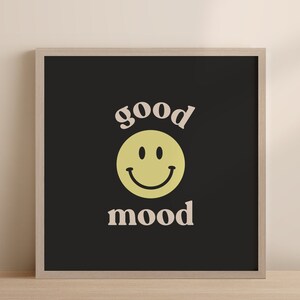 Może przedstawiać: Czarny wydruk w ramie z ż&oacute;łtą buźką i tekstem "good mood" w jasnor&oacute;żowym kolorze.