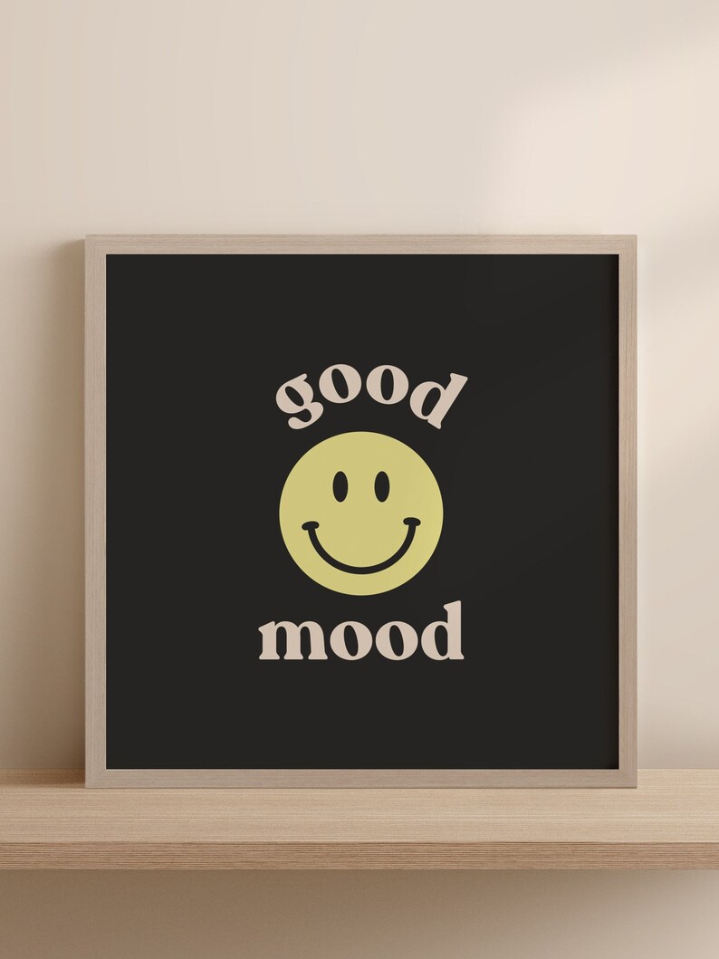 Może przedstawiać: Czarny wydruk w ramie z ż&oacute;łtą buźką i tekstem "good mood" w jasnor&oacute;żowym kolorze.