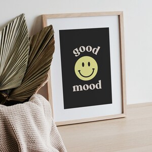 Może przedstawiać: Wydruk w ramie z czarnym tłem i białym tekstem, kt&oacute;ry brzmi "good mood" z ż&oacute;łtą buźką między słowami.