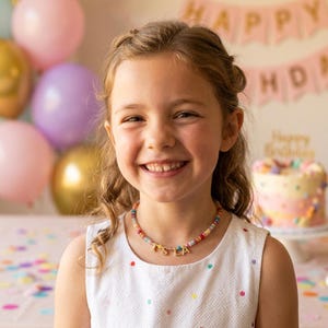 May include: A beaded necklace featuring small, multicolored round beads and gold-toned letter charms that spell out the name ISLA. The necklace is worn around the neck, resting against a white sleeveless top with small, colorful polka dots.