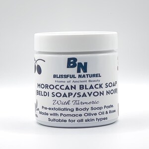 May include: A white jar with a white lid, labeled "MOROCCAN BLACK SOAP" with the text "BLISSFUL NATUREL" and "Home of Ancient Beauty". The jar also says "With Turmeric" and "Pre-exfoliating Body Soap Paste."