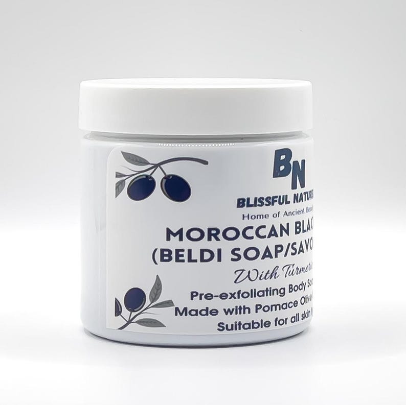 May include: A white jar with a white lid, labeled "MOROCCAN BLACK (BELDI SOAP/SAVON)" with text that reads "With Turmeric" and "Pre-exfoliating Body Soap". The jar has a logo of olives and the brand name "Blissful Nature".