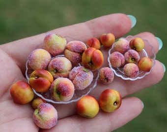 May include: A collection of miniature peaches in various shades of red and yellow, arranged in three small clear plates. The peaches are realistic and detailed, with a fuzzy texture.
