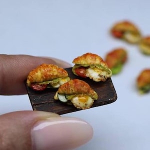 Può includere: Un vassoio da portata in legno in miniatura con tre mini panini al croissant. I panini sono farciti con lattuga, pomodoro e uovo.