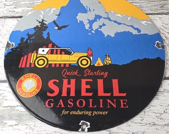 May include: A vintage Shell Gasoline sign with a circular shape. The sign features a yellow car, mountains, and the text "Quick Starting SHELL GASOLINE for enduring power." The sign has a black background with red and yellow text.