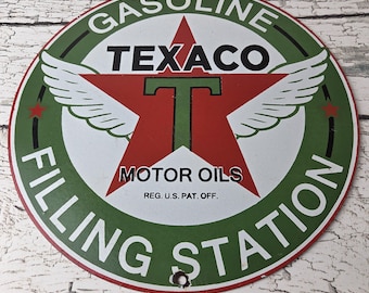 May include: A circular metal sign featuring the Texaco logo with a large red star, a green letter T, and white wings. The text reads GASOLINE, TEXACO, MOTOR OILS, REG. U.S. PAT. OFF., and FILLING STATION. The sign has a green border and white background.