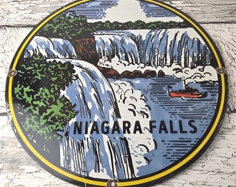 May include: Round metal sign featuring a scenic illustration of Niagara Falls. The image depicts the waterfall with blue water, green trees, and a red boat. The sign has a yellow border and the words "NIAGARA FALLS".