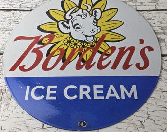 May include: Vintage Borden's Ice Cream sign. The round metal sign features a smiling cow mascot surrounded by a yellow sunflower. The words "Borden's" are in red script above "ICE CREAM" in white on a blue background.