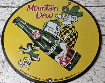 May include: A round yellow metal sign featuring a large green Mountain Dew bottle, a cartoon character in a green hat and yellow plaid shirt, and a smaller character drinking from a bottle. Text reads Mountain Dew and A PRODUCT OF PEPSI CO.