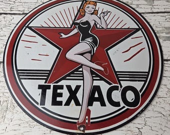 May include: A circular metal sign featuring a red star background with a graphic illustration of a person with red hair wearing a black dress and red heels. The text TEX ACO is printed in bold black capital letters across the lower portion.
