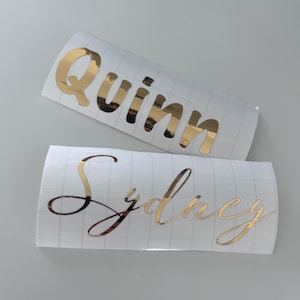 May include: Two gold vinyl stickers with names on them. The top sticker says "Quinn" and the bottom sticker says "Sydney".