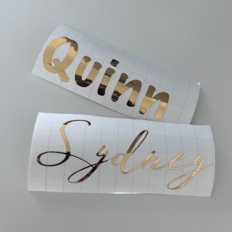May include: Two gold vinyl stickers with names on them. The top sticker says "Quinn" and the bottom sticker says "Sydney".