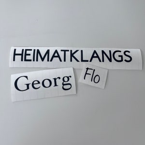May include: Three white paper labels with black text. The top label reads "HEIMATKLANGS". The middle label reads "Georg". The bottom label reads "Flo".
