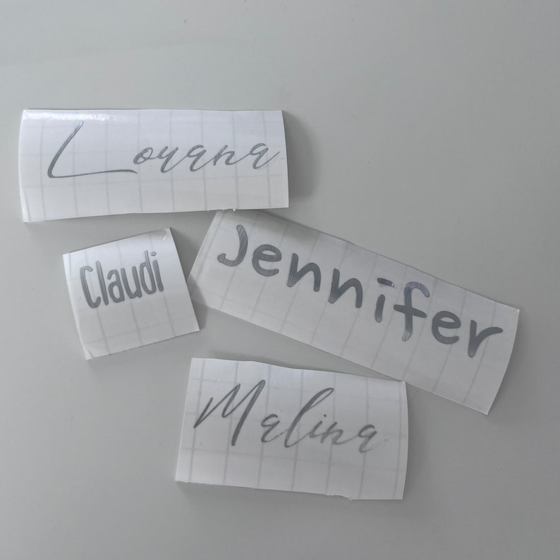 May include: Four white labels with silver lettering. The names Louana, Jennifer, Claudi, and Malina are written on the labels.