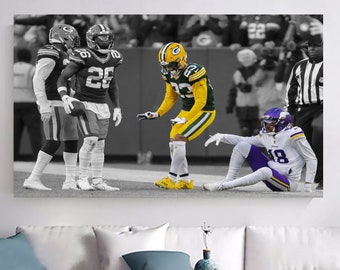 May include: A black and white photograph of a football game. A player in a green and yellow uniform is helping up a player in a purple and white uniform who is lying on the ground. The players are surrounded by other players and referees.