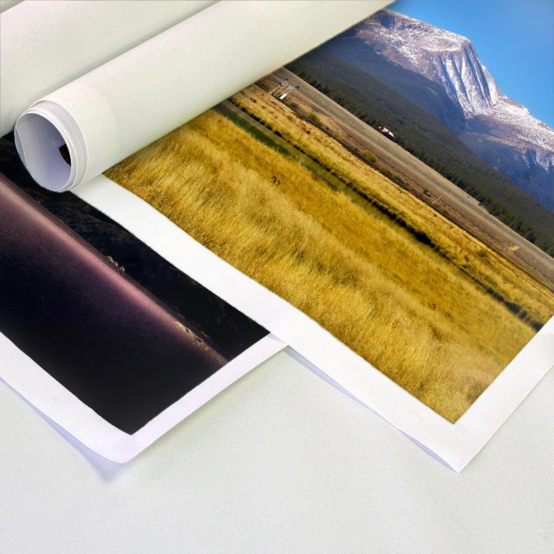 Op de afbeelding: Twee opgerolde doeken met geprinte afbeeldingen. Een doek toont een veld met hoog gras met een berg op de achtergrond. Het andere doek toont een donkere, wazige afbeelding van een watermassa.