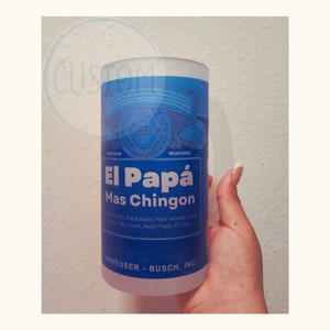 Könnte beinhalten: Eine gefrostete Glas-Tasse mit einem blauen und weißen Design. Die Tasse zeigt den Text "El Papá Mas Chingon" und den Markennamen "Anheuser-Busch, Inc."