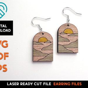 May include: A pair of laser cut wooden earrings featuring a sunset over a mountain range. The earrings are a light brown color with a yellow sun and gray mountains. The earrings are designed to be worn as a pair.