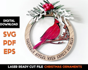 May include: Wooden Christmas ornament featuring a red cardinal perched on a branch within a circular frame. The frame has the text "CARDINALS APPEAR WHEN ANGELS ARE NEAR". The ornament is decorated with faux snow and berries. The words "DIGITAL DOWNLOAD" and "SVG PDF EPS" are also visible.
