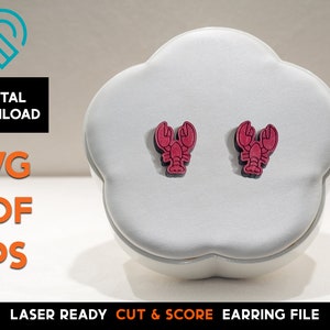 Peut inclure: Une paire de boucles d'oreilles en forme de homard rouge sur un présentoir blanc en forme de nuage. Les boucles d'oreilles sont découpées au laser et prêtes à être assemblées.