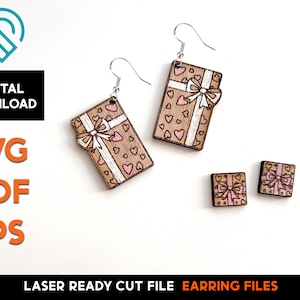 Puede incluir: Archivos de corte láser para pendientes. El diseño presenta una caja de regalo con un lazo rosa y corazones. Los pendientes están disponibles en dos tamaños, uno grande y dos más pequeños.