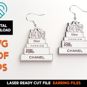 Puede incluir: Un par de pendientes de madera blanca con forma de pastel de varios pisos con las palabras "Dior Fashion", "Tom Ford" y "Chanel" en cada piso. El piso superior presenta un diseño floral.