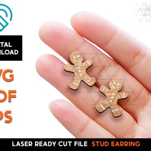 May include: Two gingerbread man stud earrings, laser cut from wood, with white icing details. The earrings are held in a hand.