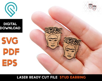 May include: A pair of laser cut wood stud earrings featuring a portrait of Frida Kahlo with a flower crown. The earrings are shown on a hand, ready to be worn.