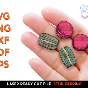 May include: A hand displays four wooden stud earrings shaped like macarons, in shades of pink and green, with a cream filling. The image also includes the text "SVG, PNG, DXF, PDF, EPS" and "LASER READY CUT FILE STUD EARRING".