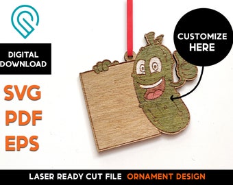 May include: Laser cut wooden ornament of a smiling pickle holding a blank sign. The sign says "Customize Here".