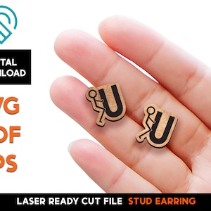 May include: A pair of laser cut wood stud earrings featuring a stick figure in a wheelchair with the letter "U" behind them. The earrings are shown on a hand.