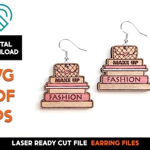 Puede incluir: Un par de pendientes de madera cortados con láser que presentan una pila de tres artículos con las palabras "MAKE UP" y "FASHION" en ellos. El artículo superior es un bolso con un corazón.