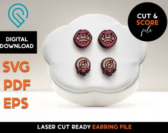 May include: Four wooden earrings with a laser-cut design. Two earrings feature open mouths with fangs, and the other two have a skull design. The earrings are displayed on a white, cloud-shaped stand. Text on the image reads "DIGITAL DOWNLOAD SVG PDF EPS" and "CUT & SCORE file".