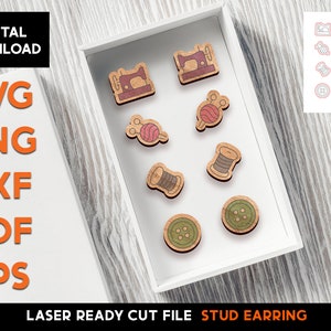 May include: A set of eight laser-cut wooden stud earrings featuring sewing-themed designs. The earrings include a sewing machine, a spool of thread, a needle and thread, and buttons. The earrings are displayed in a white box on a wooden surface.