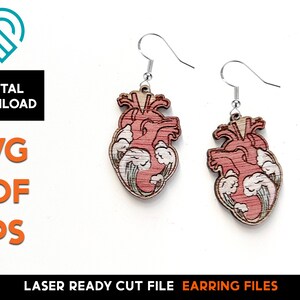 May include: A pair of laser cut wooden earrings featuring a detailed anatomical heart design with a pink and white color scheme. The earrings are attached to silver hooks.