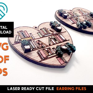 May include: Two laser cut wooden heart-shaped earrings with a bookshelf design. The earrings feature a bookshelf with books, plants, and a small animal. The earrings are ready to be assembled.