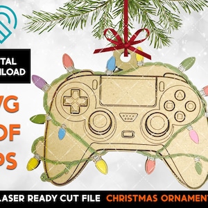 May include: A laser cut wooden Christmas ornament shaped like a video game controller with a string of colourful lights wrapped around it.