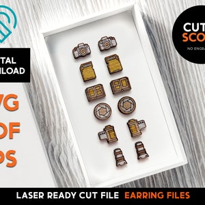 May include: A white frame with a white background displays 12 laser cut wooden earring designs. The designs include cameras, film canisters, and lenses. The text "CUT & SCORE" is visible in the upper right corner of the image.
