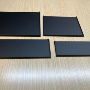 Peut inclure: Quatre plateaux rectangulaires noirs de tailles diff&eacute;rentes, dispos&eacute;s en rang&eacute;e sur une surface en bois clair.