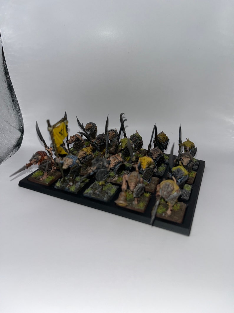 Peut inclure: Un groupe de 25 figurines de guerriers gobelins en plastique non peintes, debout sur une base noire. Les gobelins tiennent des lances et des boucliers, et certains portent des drapeaux.