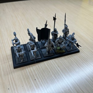 Peut inclure: Un ensemble de huit figurines miniatures non peintes, chacune sur une base noire. Les figurines sont habill&eacute;es d'une armure m&eacute;di&eacute;vale et tiennent diverses armes, notamment des &eacute;p&eacute;es, des lances et des haches. Un drapeau noir avec un &eacute;clair blanc est inclus.