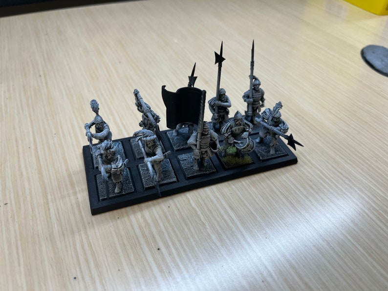 Peut inclure: Un ensemble de huit figurines miniatures non peintes, chacune sur une base noire. Les figurines sont habill&eacute;es d'une armure m&eacute;di&eacute;vale et tiennent diverses armes, notamment des &eacute;p&eacute;es, des lances et des haches. Un drapeau noir avec un &eacute;clair blanc est inclus.