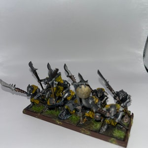 Peut inclure: Un groupe de huit figurines miniatures peintes en gris et jaune tenant des lances et des boucliers. Les figurines sont debout sur une base brune avec de l'herbe verte.
