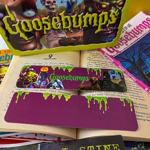 May include: A stack of Goosebumps books with a green, purple, and pink bookmark. The bookmark features a monster with green slime dripping from its head. The text on the bookmark reads "Goosebumps".