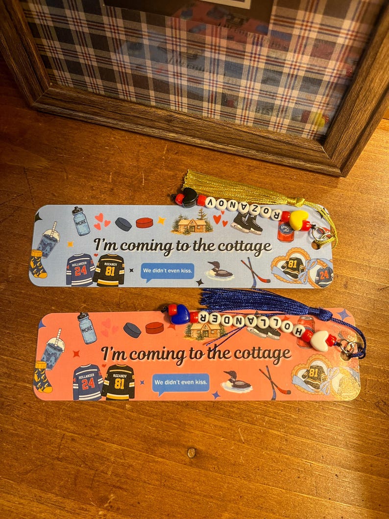 May include: Two decorative bookmarks with tassels. One is light blue, the other is coral. Both feature hockey-themed graphics, the text "I'm coming to the cottage", and the text "We didn't even kiss."