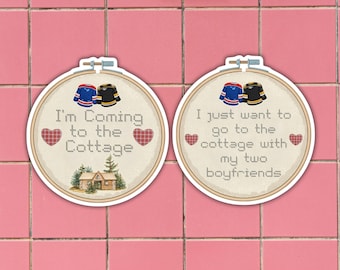 May include: Two round stickers with cross-stitch designs. One says "I'm Coming to the Cottage" with a cabin illustration and hearts. The other says "I just want to go to the cottage with my two boyfriends". Each has hockey jerseys.