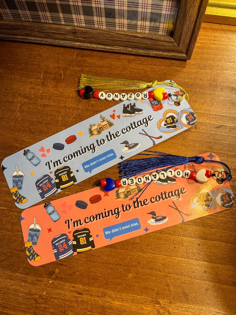 May include: Two decorative bookmarks with tassels and beaded accents. One is light blue, the other is coral. Both feature hockey-themed illustrations, text that reads "I'm coming to the cottage," and the names ROZANOV and HOLLANDER.