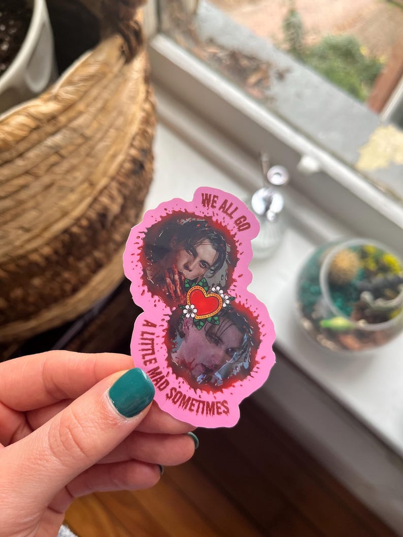May include: Pink sticker with two images of a person with blood splatters around them. The text on the sticker reads "We all go a little mad sometimes".
